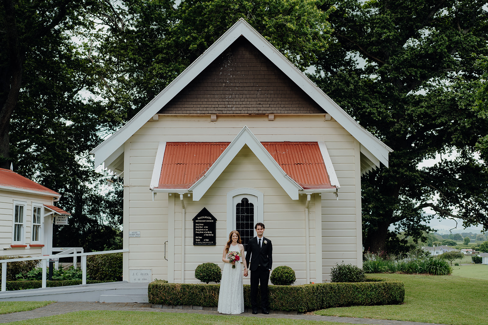 A bride and groom standing in front of the church at the Firth Tower and Museum, a Matamata Wedding Venue being photographed by Waikato Photographer Haley Adele Photography