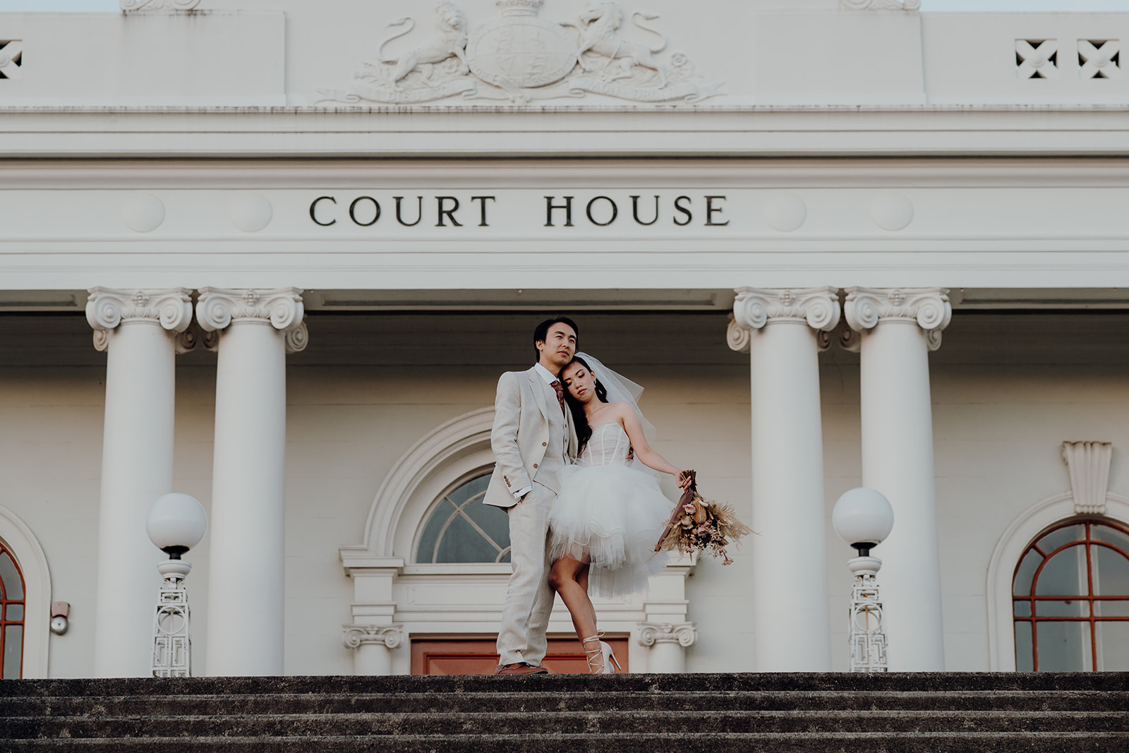 A bride and groom standing in front of the Courthouse in Hamilton City having wedding portraits taken by Waikato Photographer Haley Adele Photography