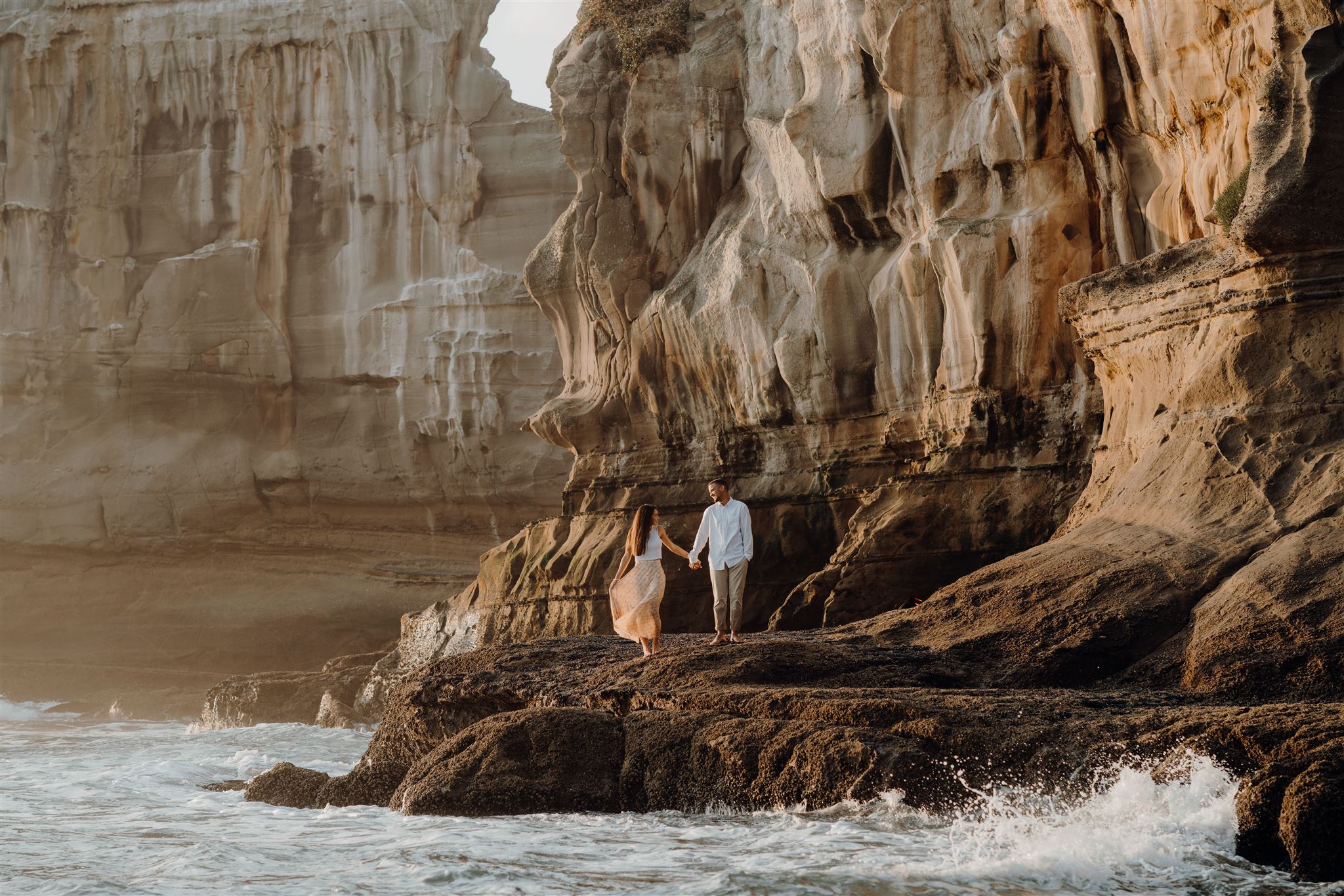 A couple standing on the rocks at Maukatia Bay in Auckland during an engagement photoshoot, being photographed by Waikato and Bay of Plenty Photographer Haley Adele Photography