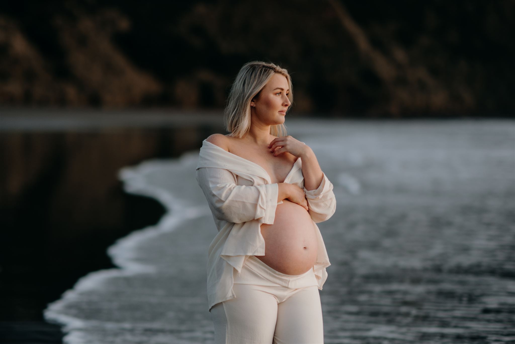 A pregnant woman being photographed at Raglan Beach during a maternity photoshoot by Haley Adele Photography