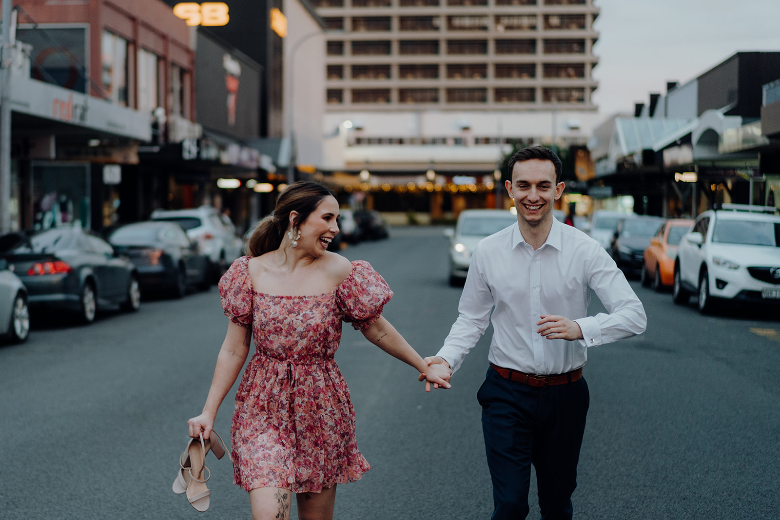 A couple running down a city street during an engagement photoshoot in Hamilton City, being photographed by Waikato and Bay of Plenty Wedding Photographer Haley Adele Photography