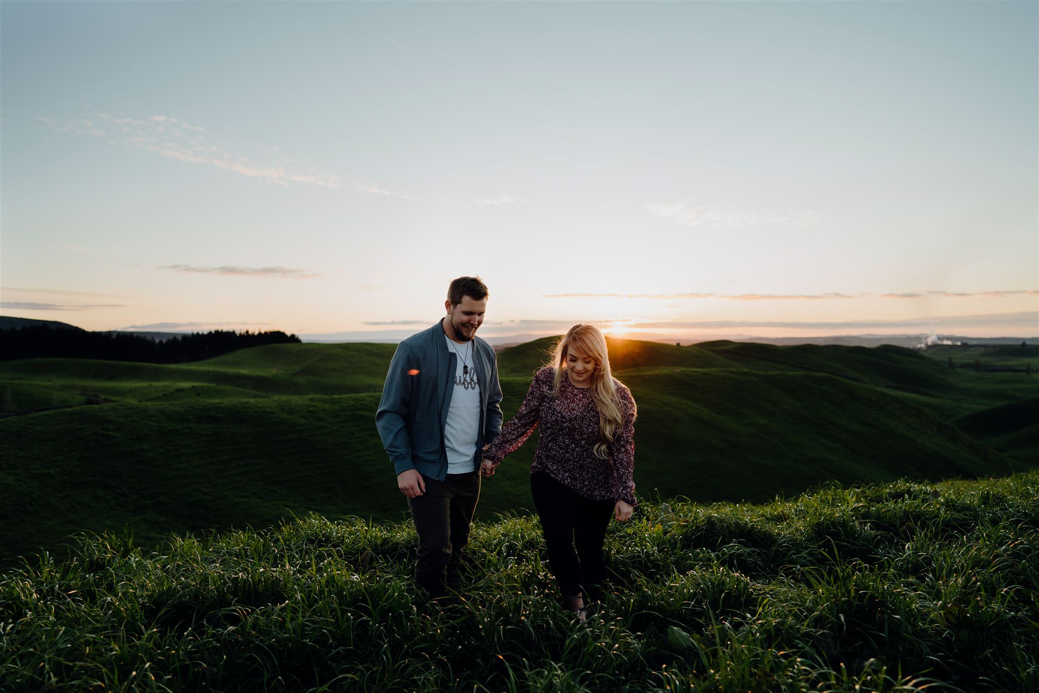 A couple walking through lush green grass during an engagement photoshoot with Waikato Photographer Haley Adele Photography