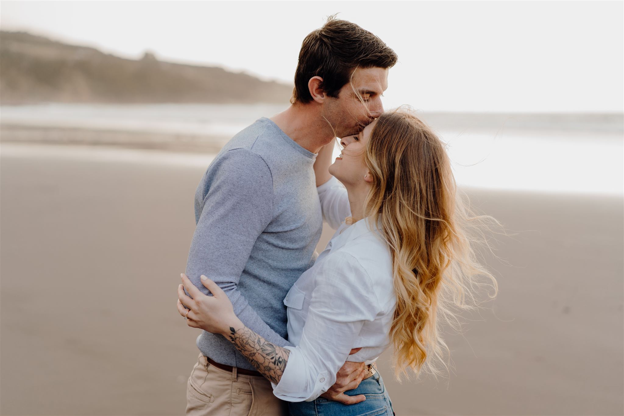A couple hugging on Ngarunui Beach in Waikato during their engagement photoshoot being photographed by Waikato Photographer Haley Adele Photography