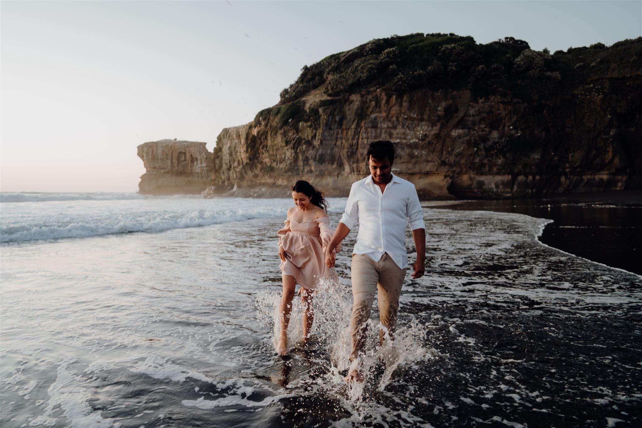 A couple walking along the beach in muriwai being photographed by Waikato & Bay of Plenty Photographer Haley Adele Photography