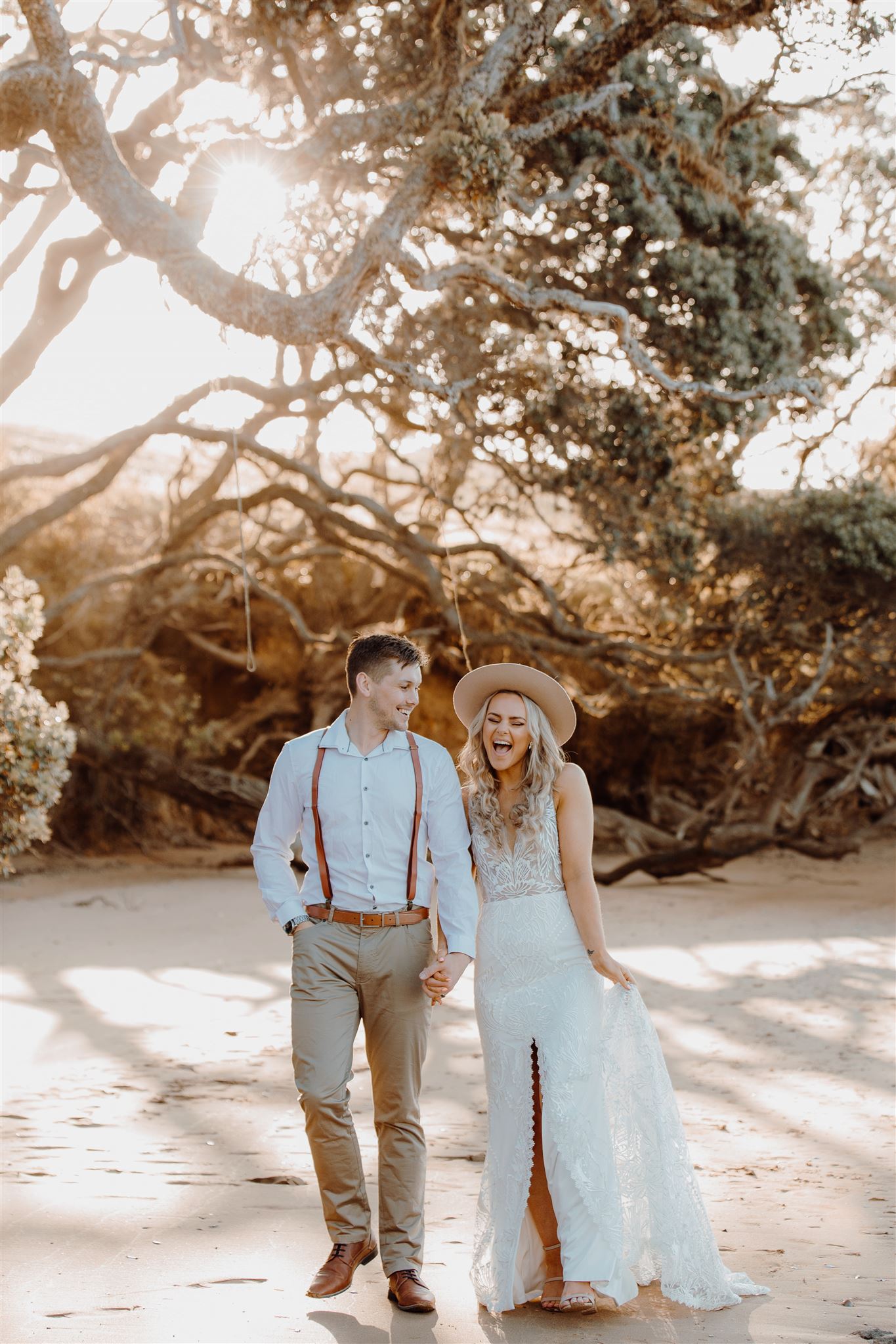 A couple wearing boho wedding vibes walking along the private beach at northland wedding venue Baylys Farm, photographed by Haley Adele Photography