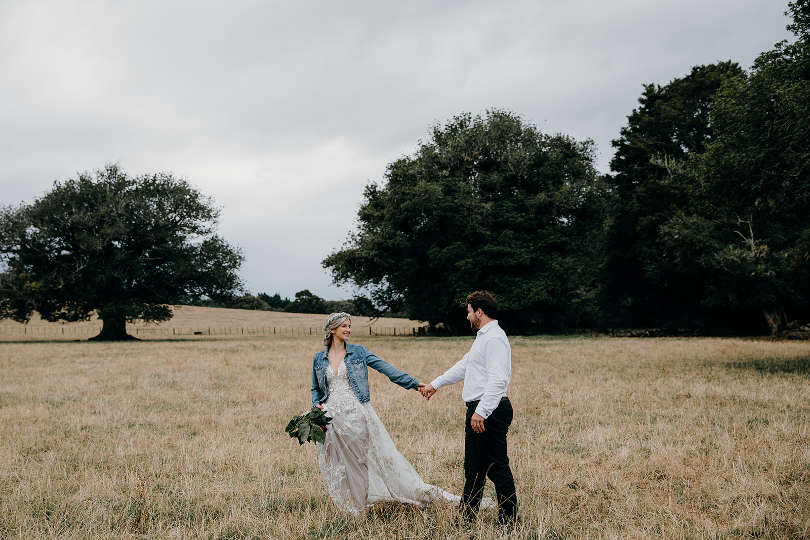 A couple walking in a field of grass at Waikato North Show Grounds during their wedding photoshoot, being photographed by Waikato and Bay of Plenty wedding photographer Haley Adele Photography