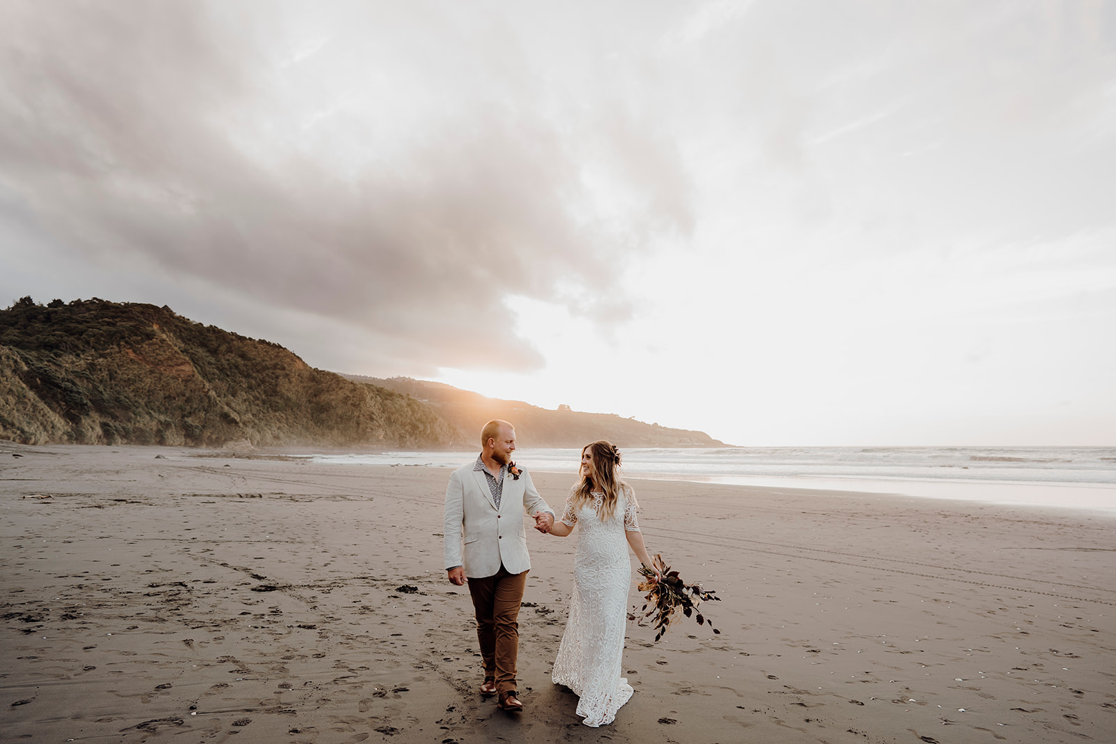 A wedding couple walking along Ngarunui Beach with it's black sand and low tides, photographed by Haley Adele Photography