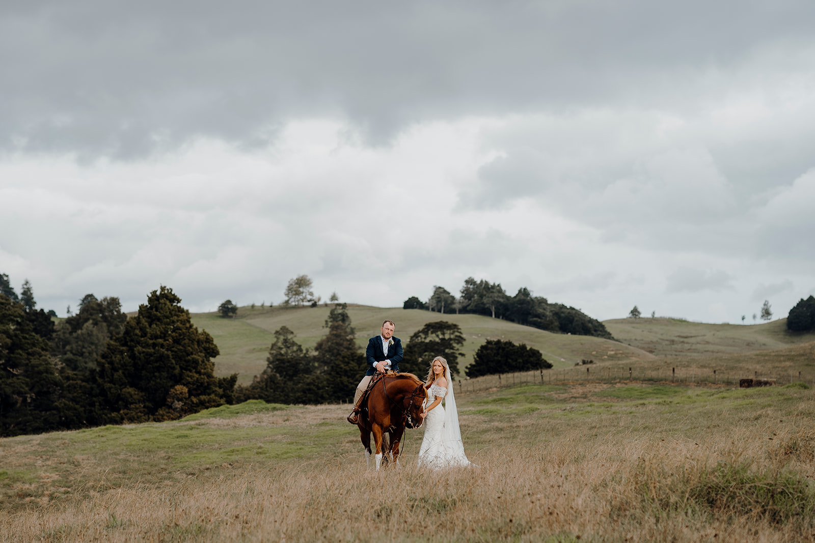 A bride standing next to a horse that a groom is sitting on during a wedding portrait photoshoot in northland where the couple have just gotten married