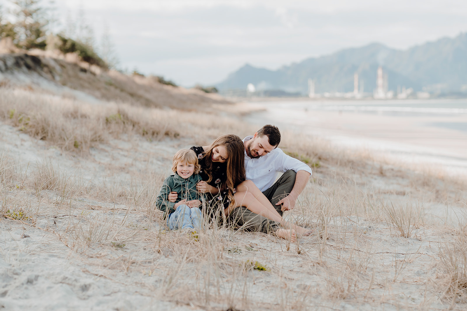 A family sitting and smiling on Ruakaka Beach in Whangarei during a family photoshoot by Waikato Photographer Haley Adele.