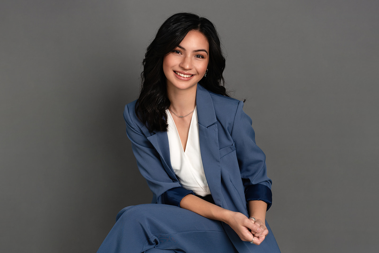 Zian wearing a blue suit sitting against a grey backdrop during her commercial headshot shoot in hamilton by haley adele photography