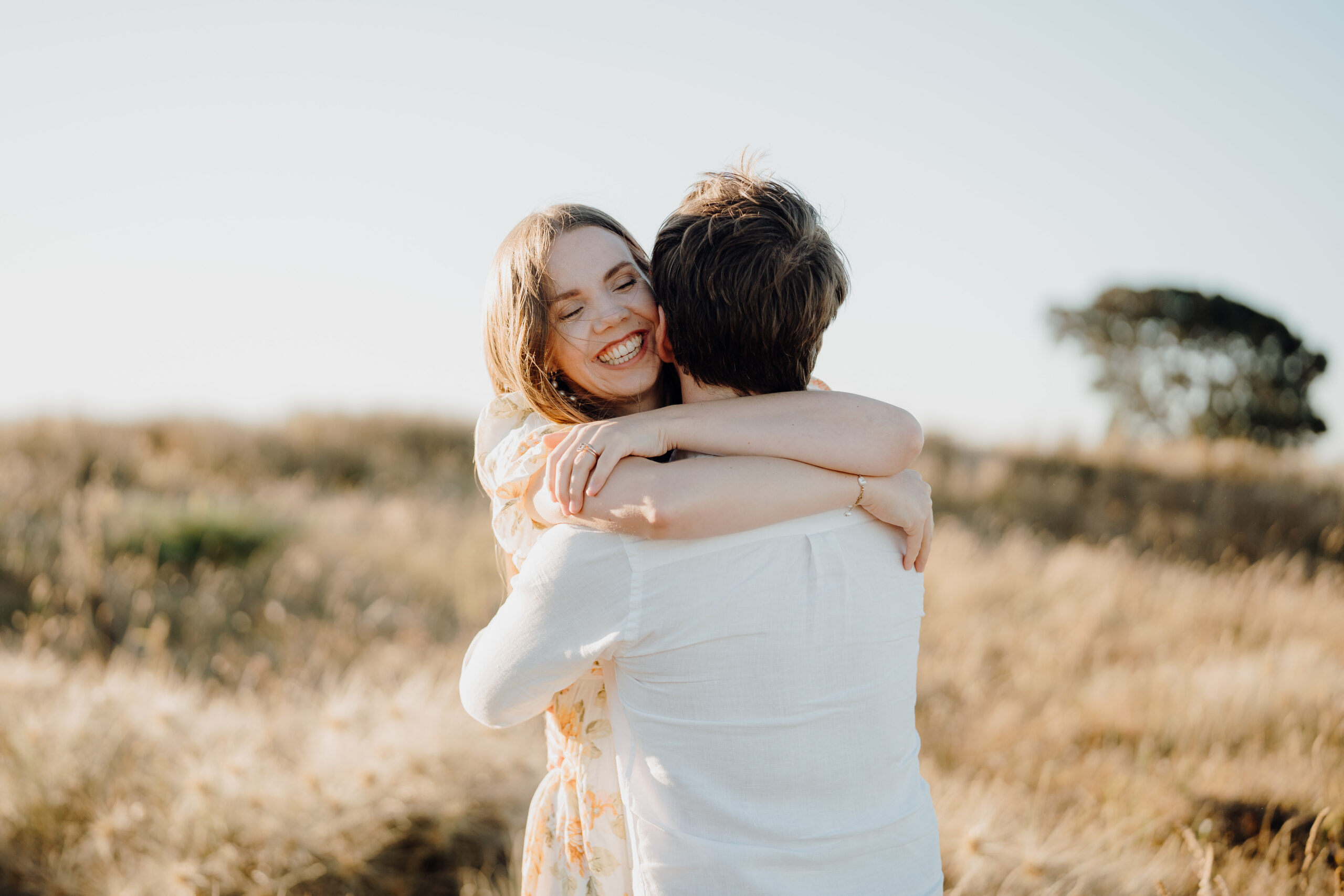 Lysanah and Nick during their Waihi Beach couple shoot at sunset, hugging and laughing together on the sand.