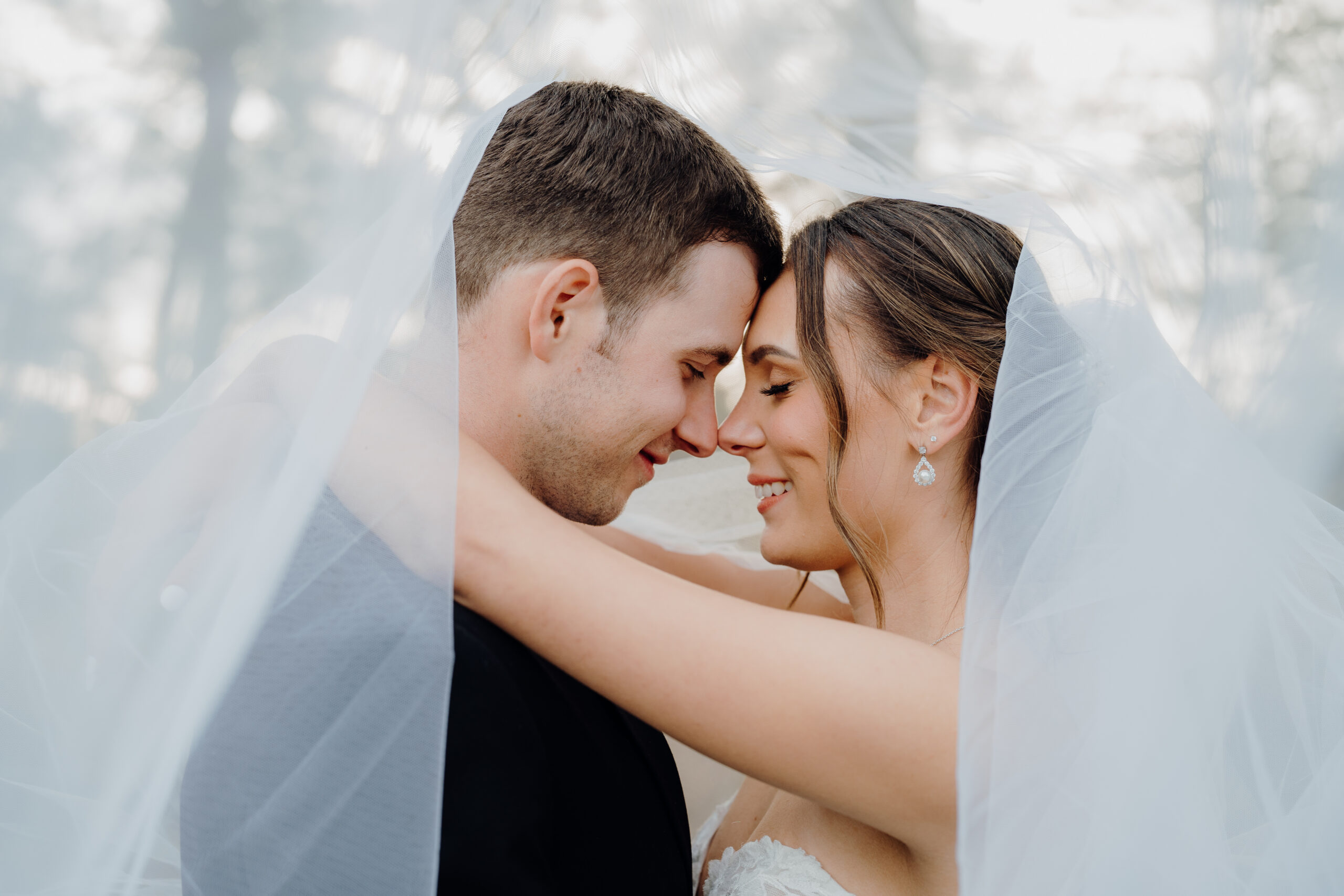 Close-up of Tiffany and Josh at their Tree Church wedding, draped under the veil with the sunset behind them, eyes closed and noses touching.